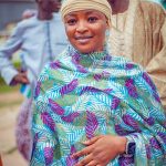 A woman in colorful traditional attire smiles during a cultural gathering outdoors.