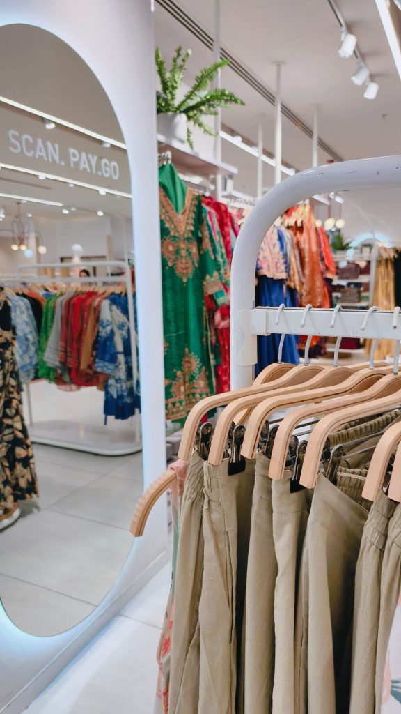 Chic clothing store showcasing vibrant dresses and neutral pants, with a scan-pay-go feature.